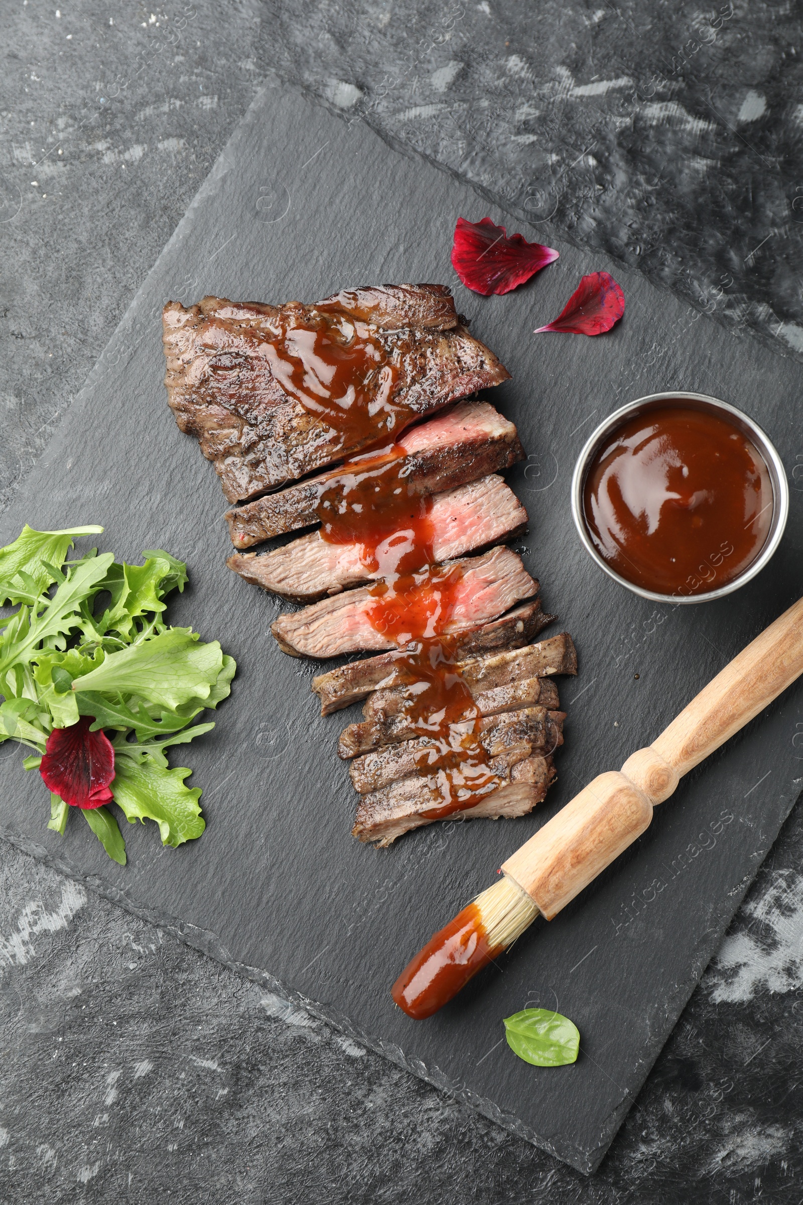 Photo of Pieces of delicious roasted beef meat with sauce and greens on black table, top view