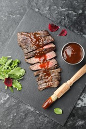 Photo of Pieces of delicious roasted beef meat with sauce and greens on black table, top view