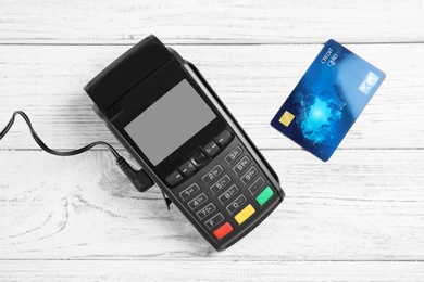 Photo of Modern payment terminal and credit card on white wooden background, top view
