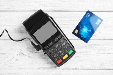 Modern payment terminal and credit card on white wooden background, top view