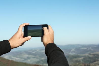 Man taking photo of beautiful mountain landscape with smartphone