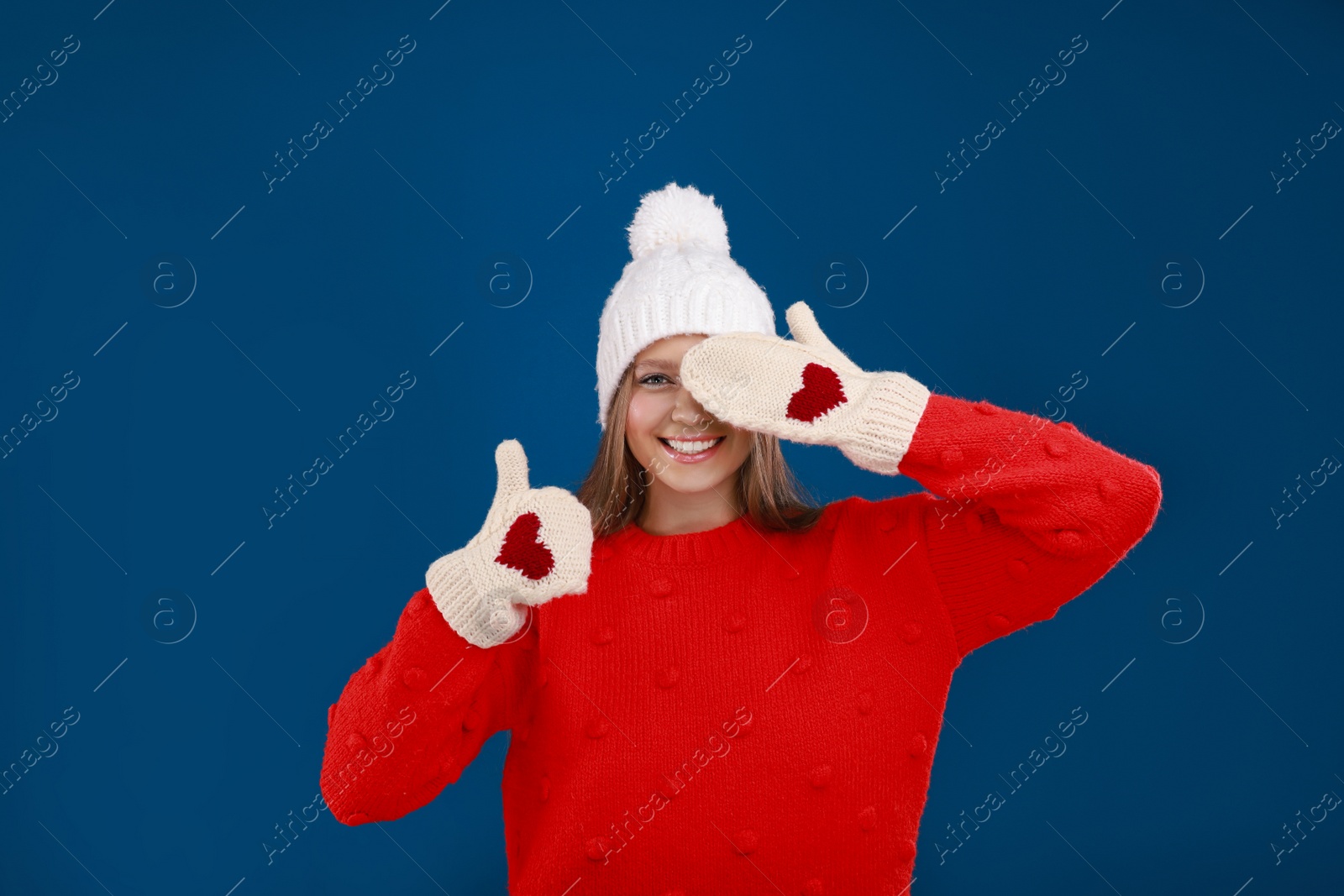 Photo of Young woman in warm sweater, mittens and hat on blue background. Winter season