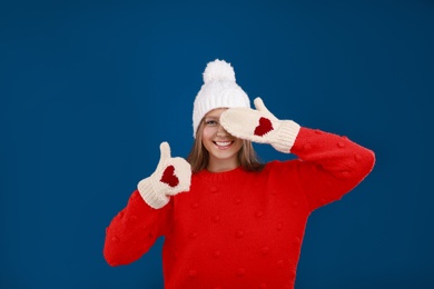 Photo of Young woman in warm sweater, mittens and hat on blue background. Winter season