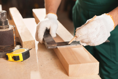 Professional carpenter working with wooden board at workbench, closeup
