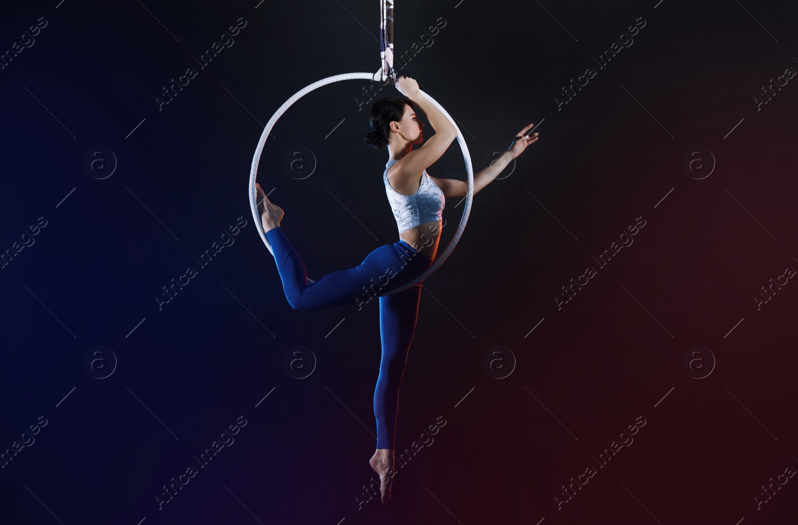 Photo of Young woman performing acrobatic element on aerial ring indoors