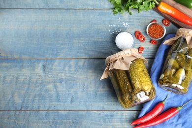 Flat lay composition with jars of pickled cucumbers on blue wooden table, space for text