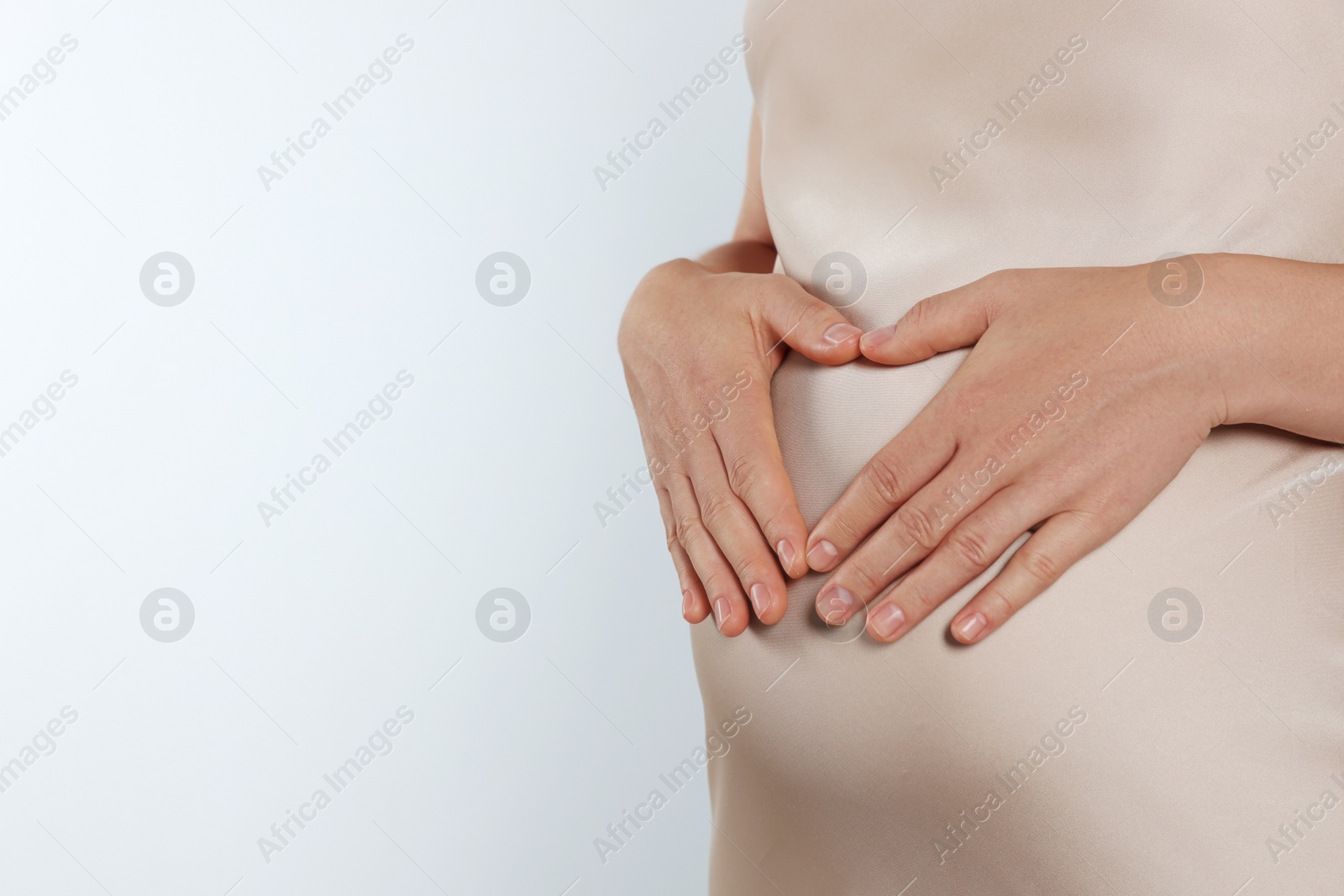Photo of Pregnant woman making heart with her hands on light grey background, closeup. Space for text