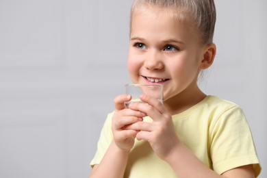 Happy little girl holding glass of fresh water on grey background, space for text