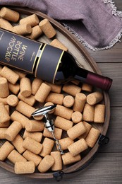 Photo of Tray with corkscrew, wine bottle and stoppers on wooden table, flat lay