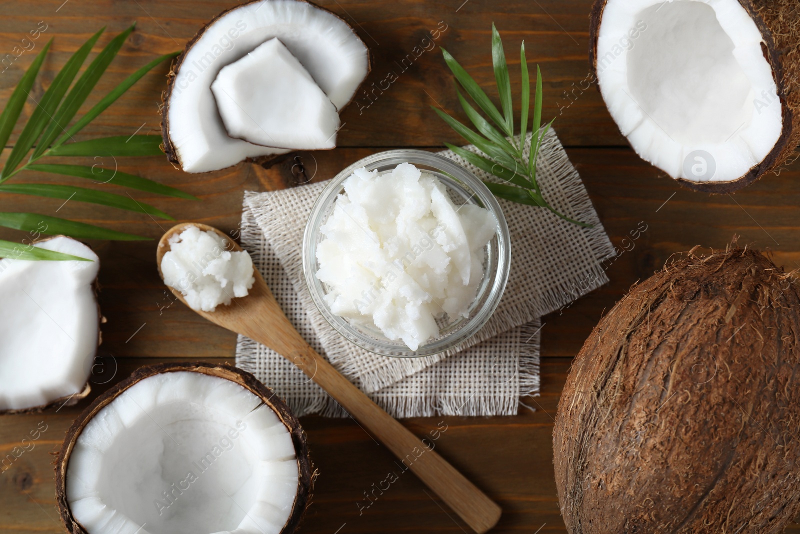 Photo of Organic coconut cooking oil, fresh fruits and leaves on wooden table, flat lay