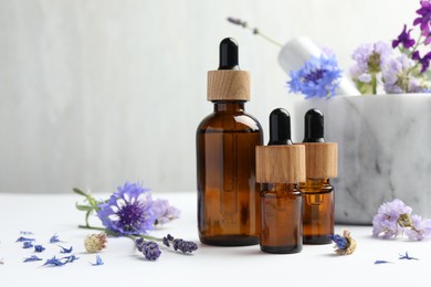 Aromatherapy. Essential oils, flowers, mortar and pestle on white table