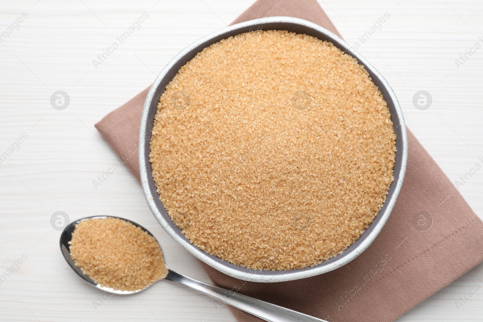 Photo of Brown sugar in bowl and spoon on white wooden table, flat lay