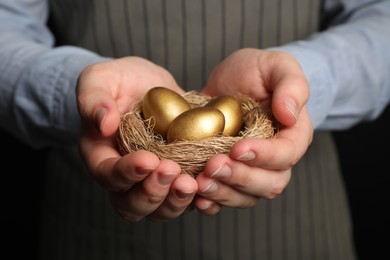 Photo of Woman holding nest with shiny golden eggs on black background, closeup