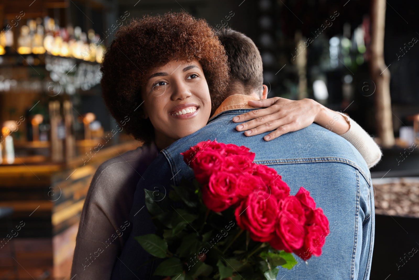 Photo of International dating. Beautiful woman with bouquet of roses hugging her boyfriend in cafe