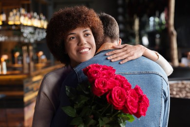International dating. Beautiful woman with bouquet of roses hugging her boyfriend in cafe