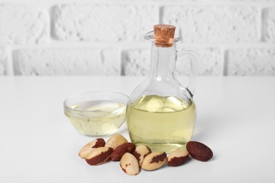 Photo of Tasty Brazil nuts and oil on white table against brick wall