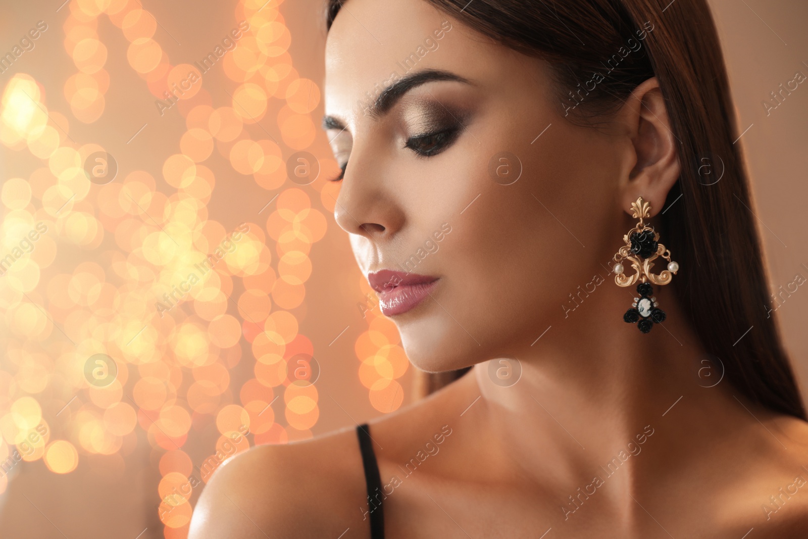 Photo of Beautiful young woman with elegant jewelry against defocused lights. Space for text