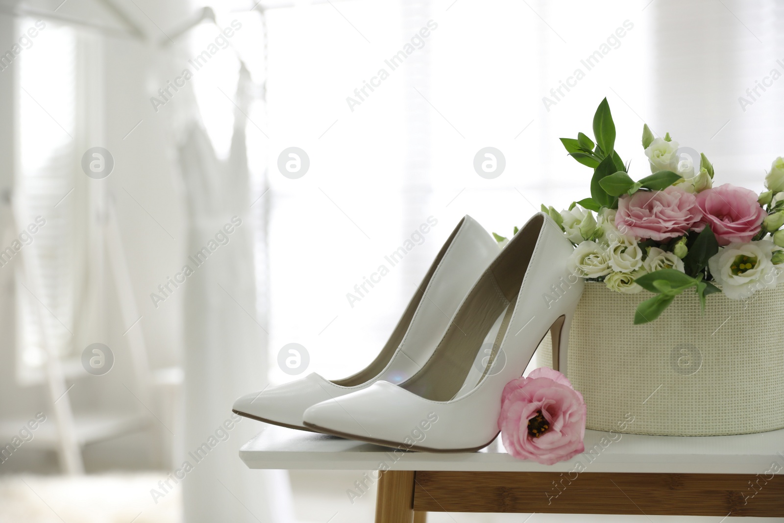 Photo of Pair of white high heel shoes, flowers and blurred wedding dress on background, space for text