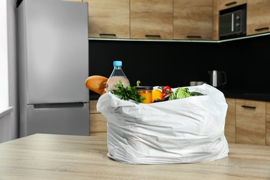 Photo of Plastic bag with vegetables and other products on wooden table in kitchen. Space for text