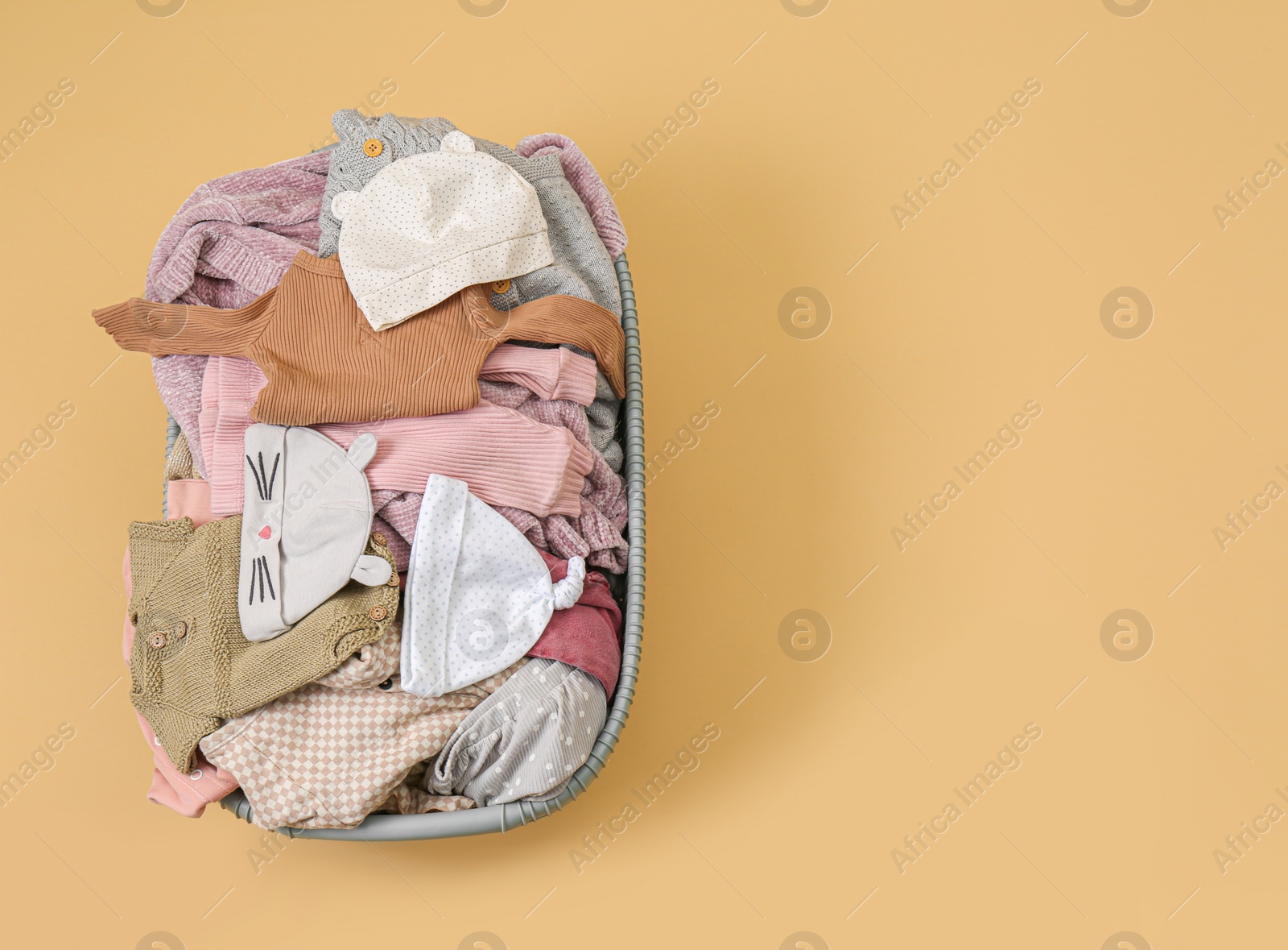 Photo of Laundry basket with baby clothes on light brown background, top view. Space for text