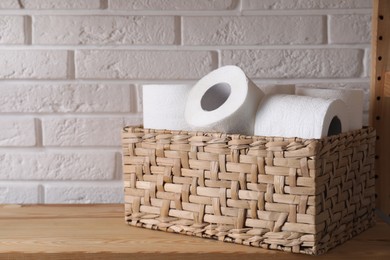Photo of Toilet paper rolls in wicker basket on wooden shelf against white brick wall, space for text