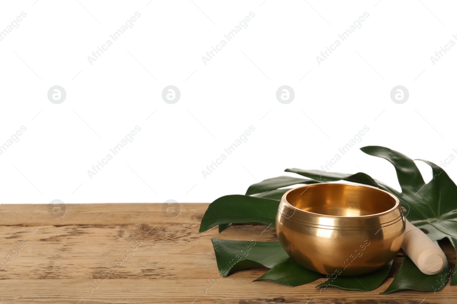 Photo of Golden singing bowl, mallet and monstera leaf on wooden table against white background, space for text