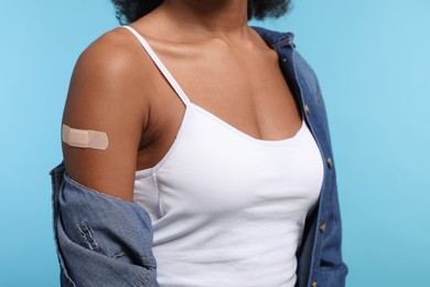 Photo of Young woman with adhesive bandage on her arm after vaccination against light blue background, closeup