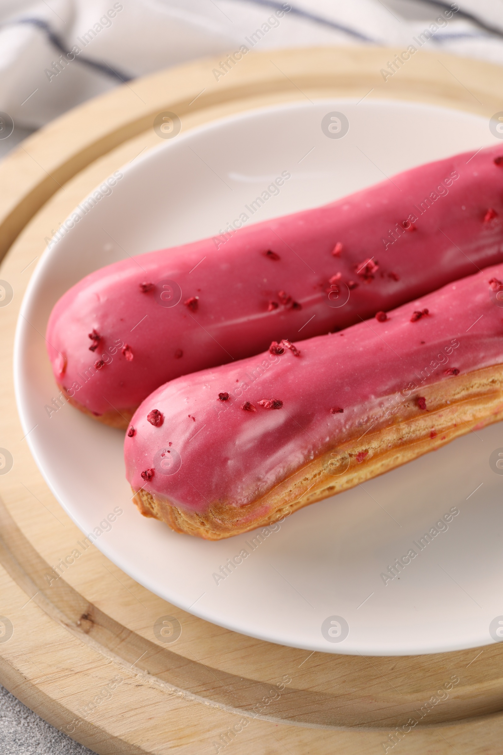 Photo of Plate with tasty glazed eclairs on wooden board, closeup