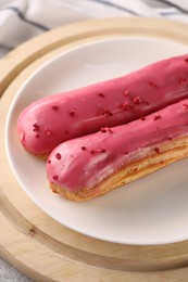 Photo of Plate with tasty glazed eclairs on wooden board, closeup