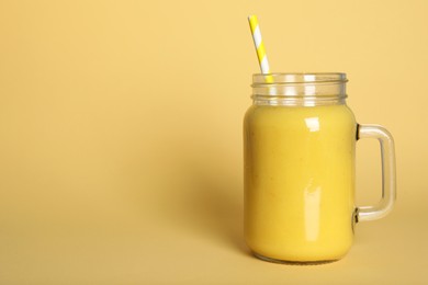 Photo of Mason jar of tasty smoothie with straw on beige background. Space for text
