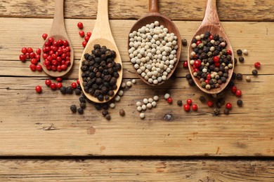 Aromatic spice. Different peppers in spoons on wooden table, flat lay. Space for text