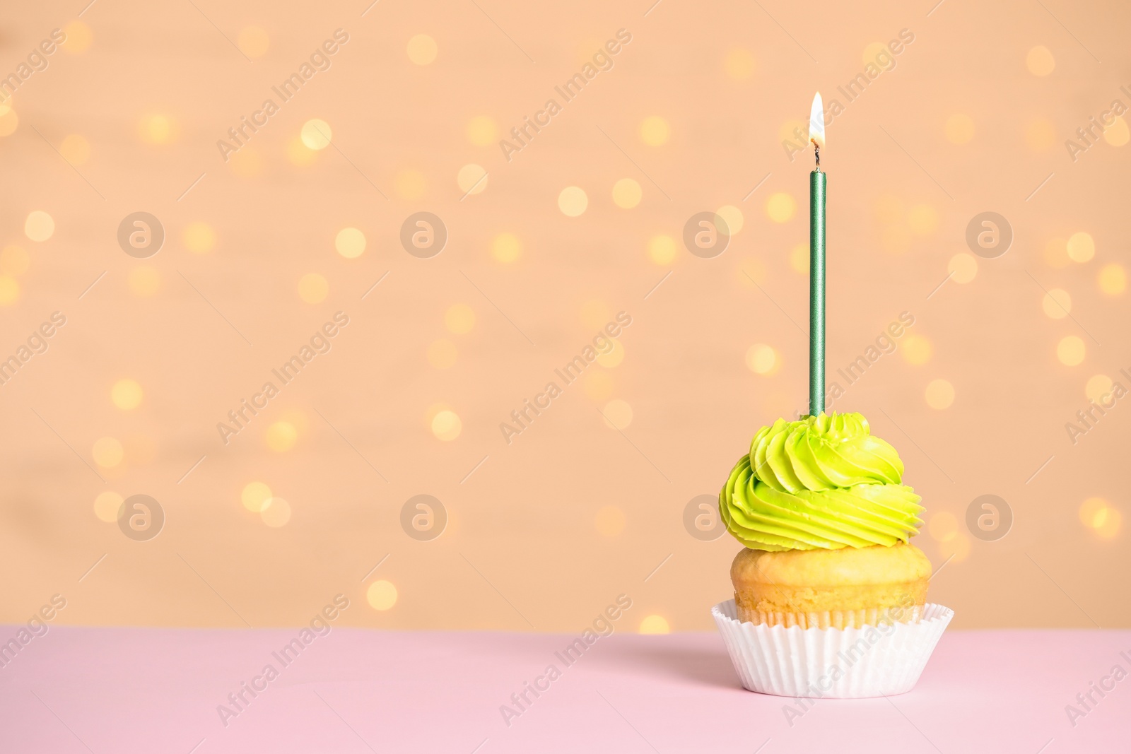 Photo of Birthday cupcake with candle on table against festive lights