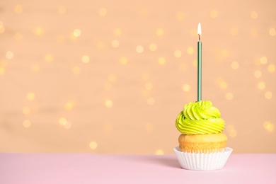 Birthday cupcake with candle on table against festive lights
