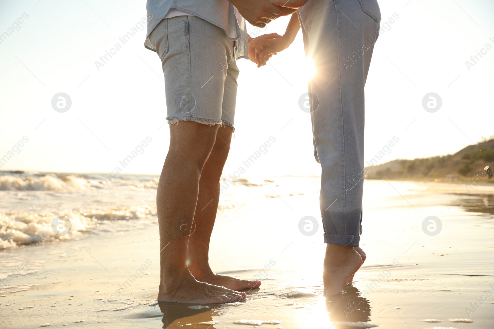 Photo of Couple on sandy beach near sea at sunset, closeup of legs