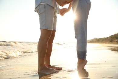 Photo of Couple on sandy beach near sea at sunset, closeup of legs