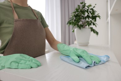 Photo of Woman with microfiber cloth cleaning white table in room, closeup