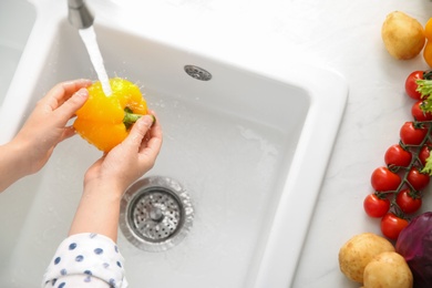 Photo of Woman washing fresh yellow bell pepper in kitchen sink, top view