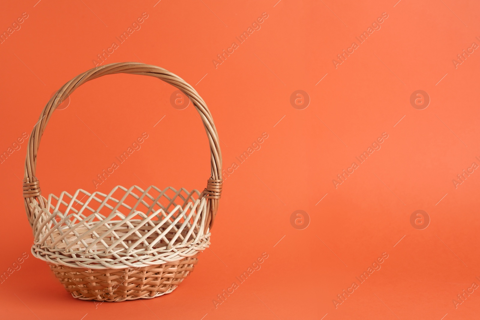 Photo of Empty wicker basket on coral background, space for text. Easter item