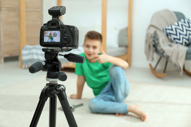 Photo of Cute little blogger recording video at home, focus on camera
