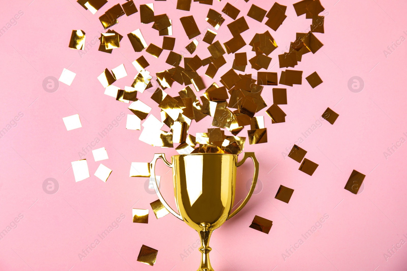 Photo of Gold trophy cup and confetti on light pink background, flat lay