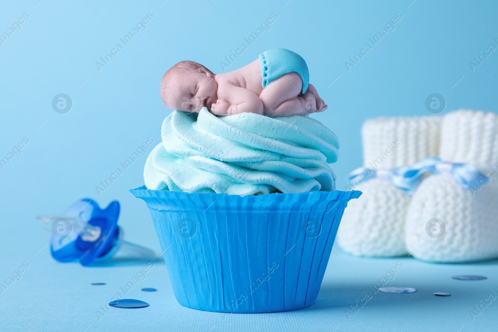 Photo of Beautifully decorated baby shower cupcake with cream and boy topper on light blue background, closeup