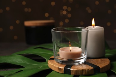 Burning candles with tropical leaf on table, space for text. Bokeh effect