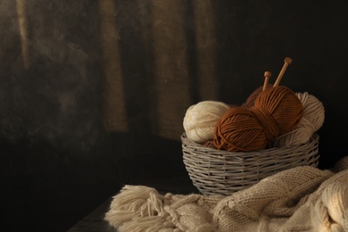 Photo of Woolen yarns in basket on dark background. Space for text