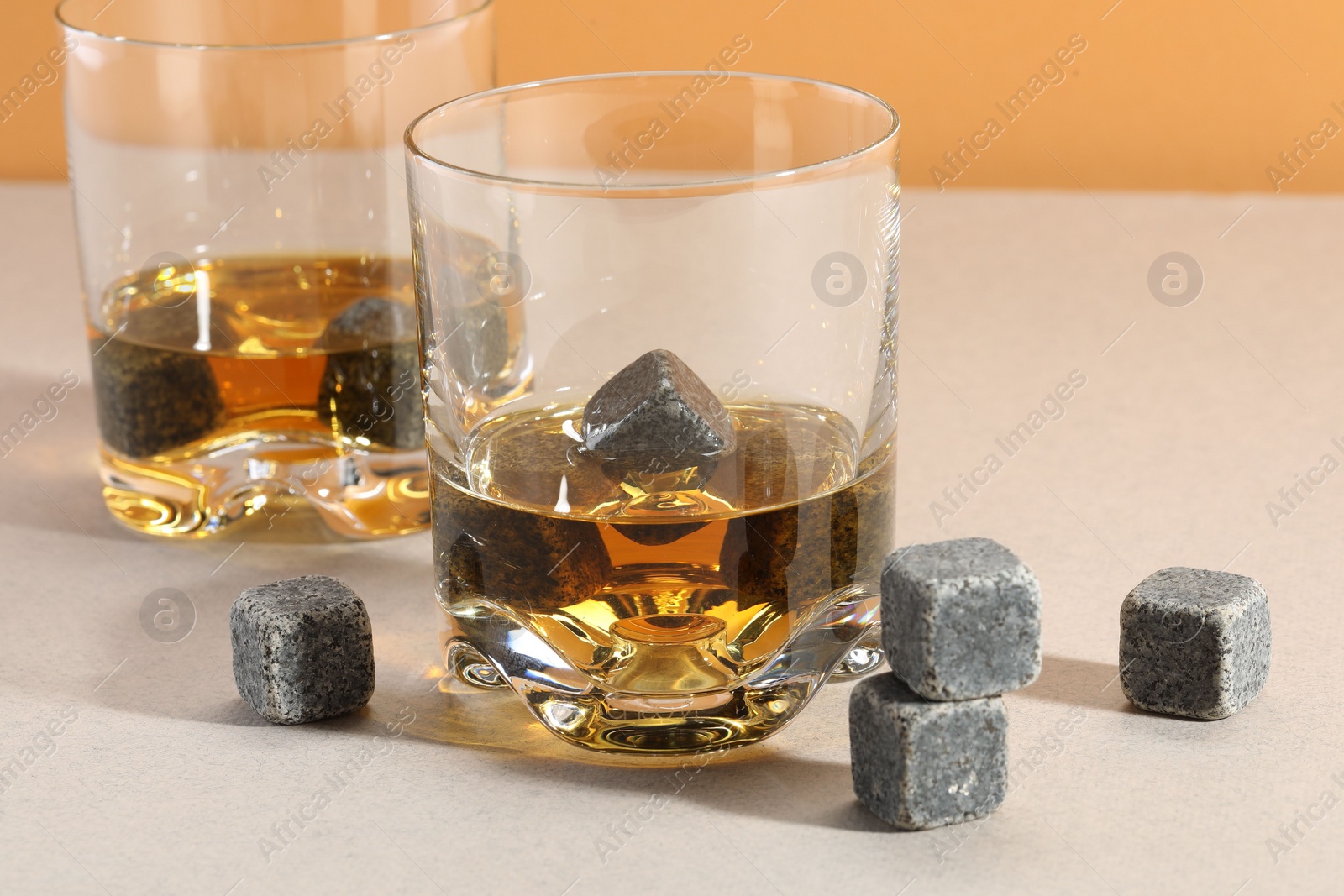 Photo of Whiskey stones and drink in glasses on light table, closeup