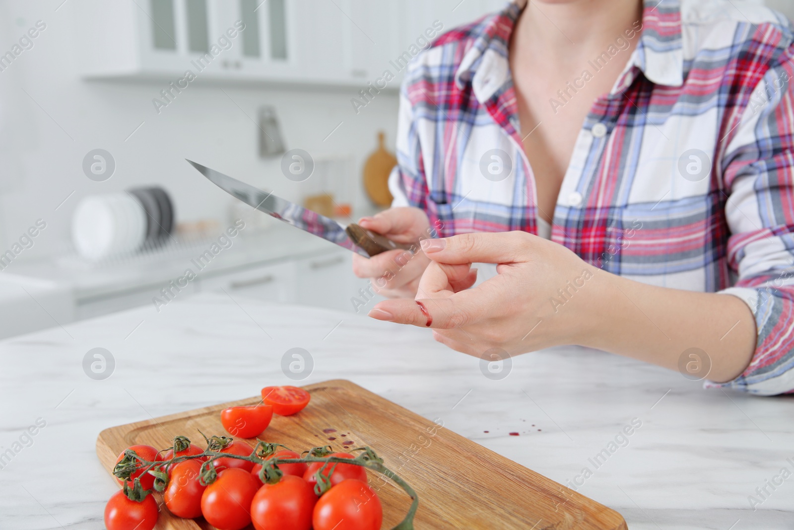 Photo of Woman cut finger with knife while cooking in kitchen, closeup