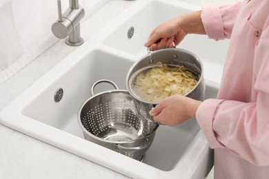 Woman draining pasta into colander at sink, closeup