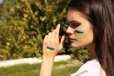 Photo of Young woman with drawings of Ukrainian flag outdoors, closeup. Space for text