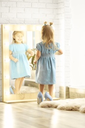 Cute little girl wearing high heeled shoes at home