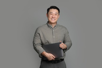 Portrait of happy businessman with laptop on grey background