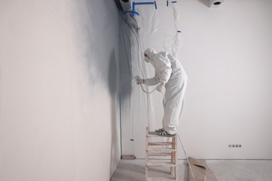 Decorator dyeing wall in grey color with spray paint indoors